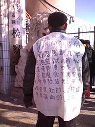 Бащата на Джоу Шянгянг (Zhou Xiangyang) с фланелка, чийто надпис осъжда преследването на сина му и призовава за неговото освобождаване. 